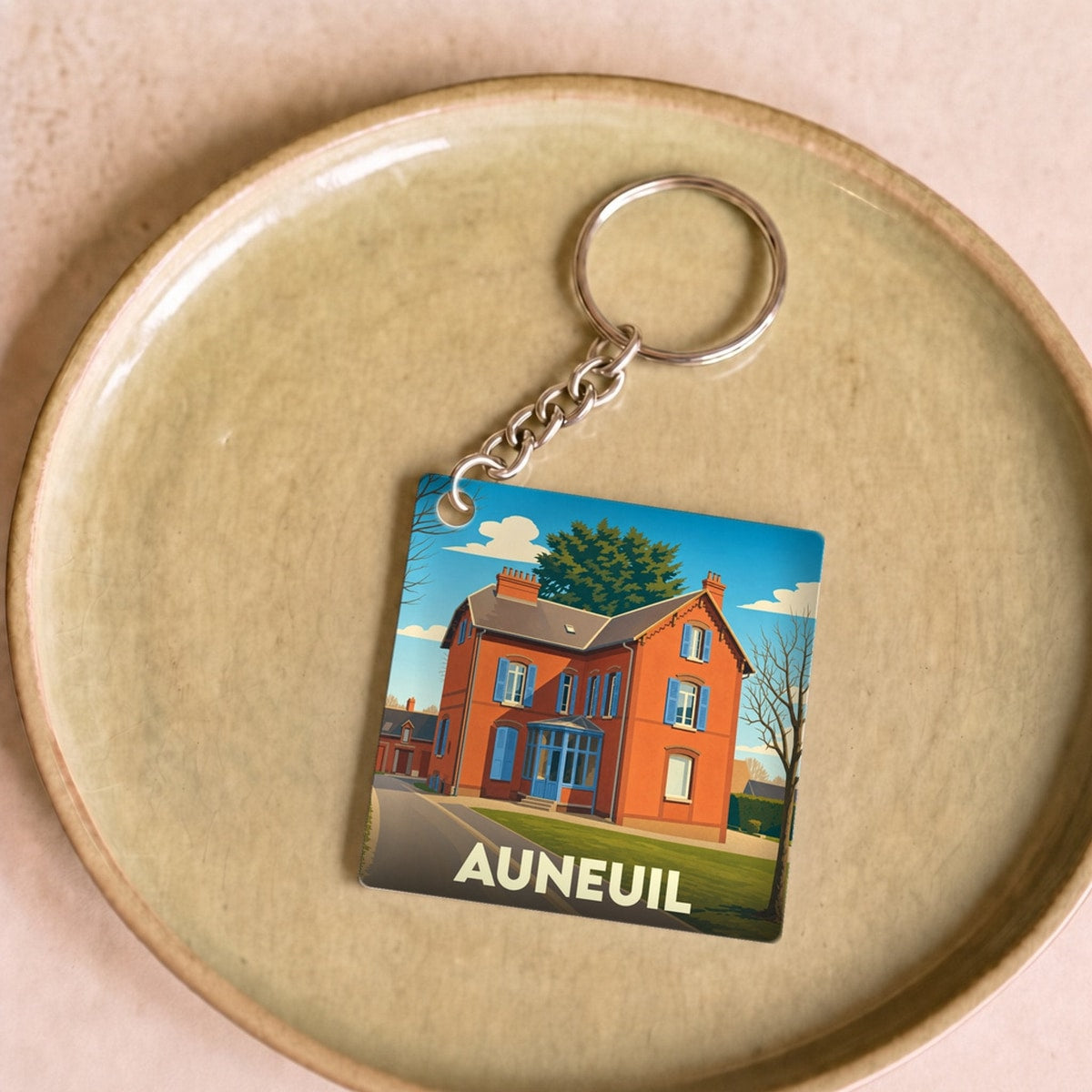 Porte-clés souvenir de la ville de Auneuil avec une illustration stylisée d'une maison traditionnelle.