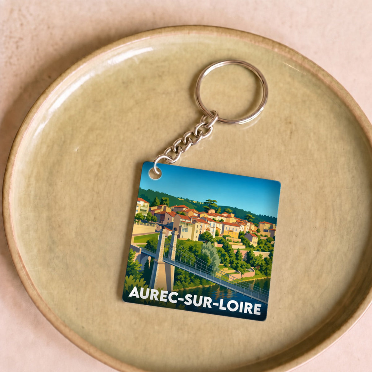 Porte-clés souvenir de la ville d'Aurec-sur-Loire avec une illustration stylisée de son pont et de ses maisons au bord de l'eau.