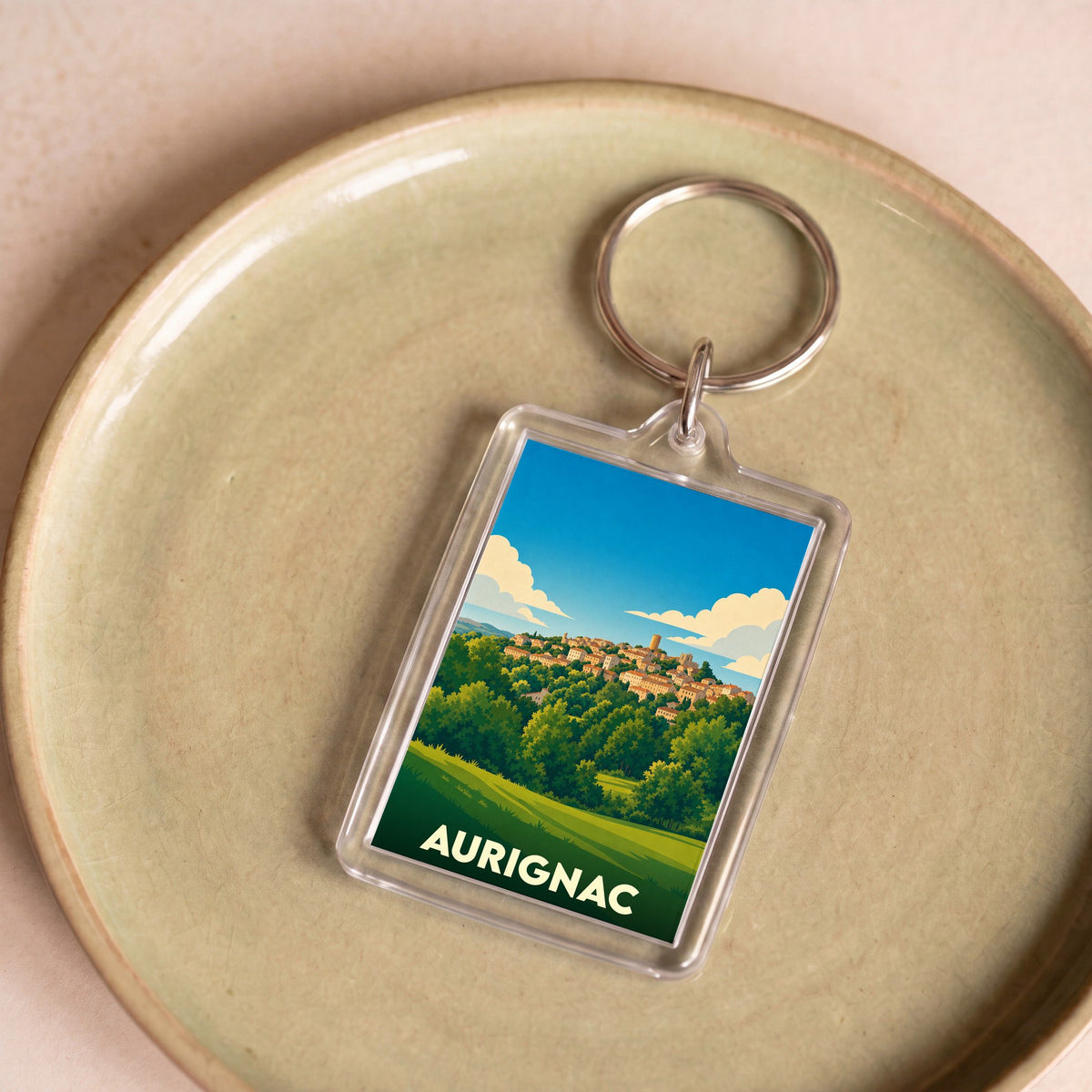 Porte-clés souvenir de la ville d'Aurignac avec une illustration stylisée de son paysage vallonné.