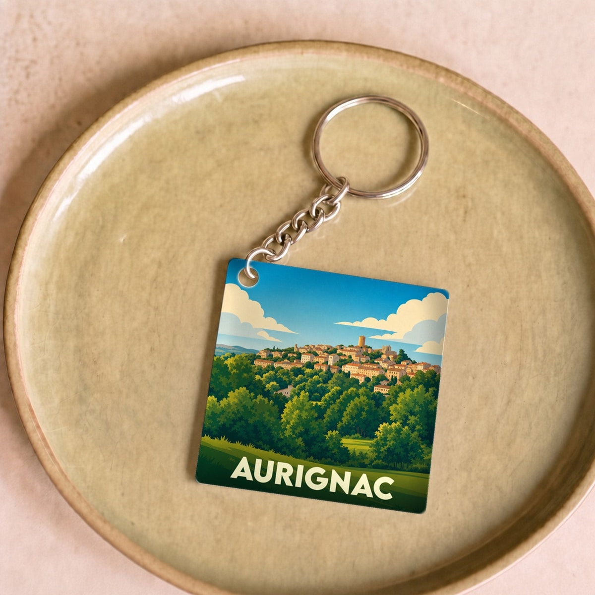 Porte-clés souvenir de la ville d'Aurignac avec une illustration stylisée de son paysage vallonné.