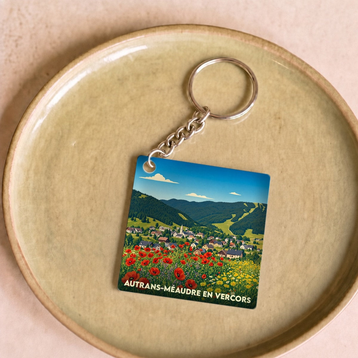 Porte-clés souvenir de la ville d'Autrans-Méaudre en Vercors avec une illustration stylisée d'un paysage de montagne fleuri.