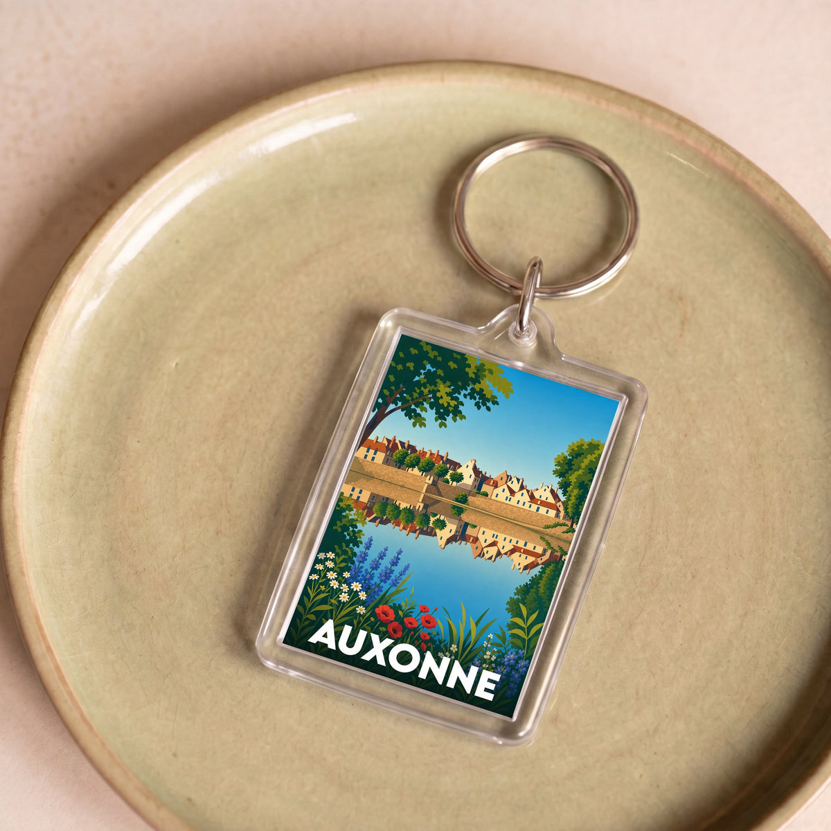 Porte-clés souvenir de la ville d'Auxonne avec une illustration stylisée d'un paysage urbain au bord de l'eau.