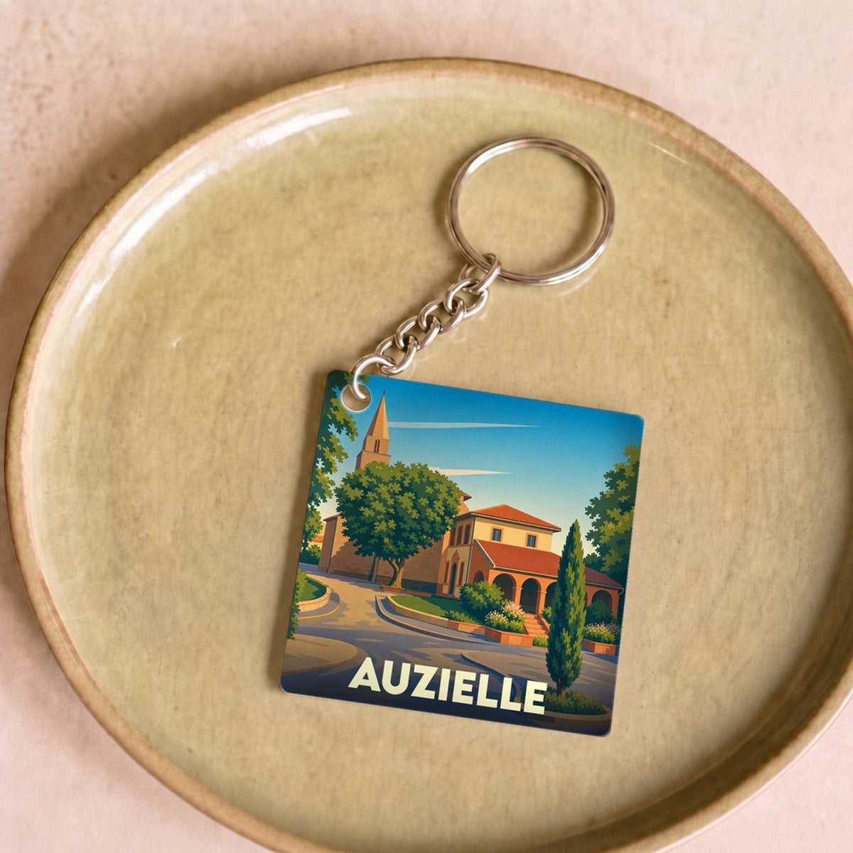 Porte-clés souvenir de la ville d'Auzielle avec une illustration stylisée d'un paysage urbain.