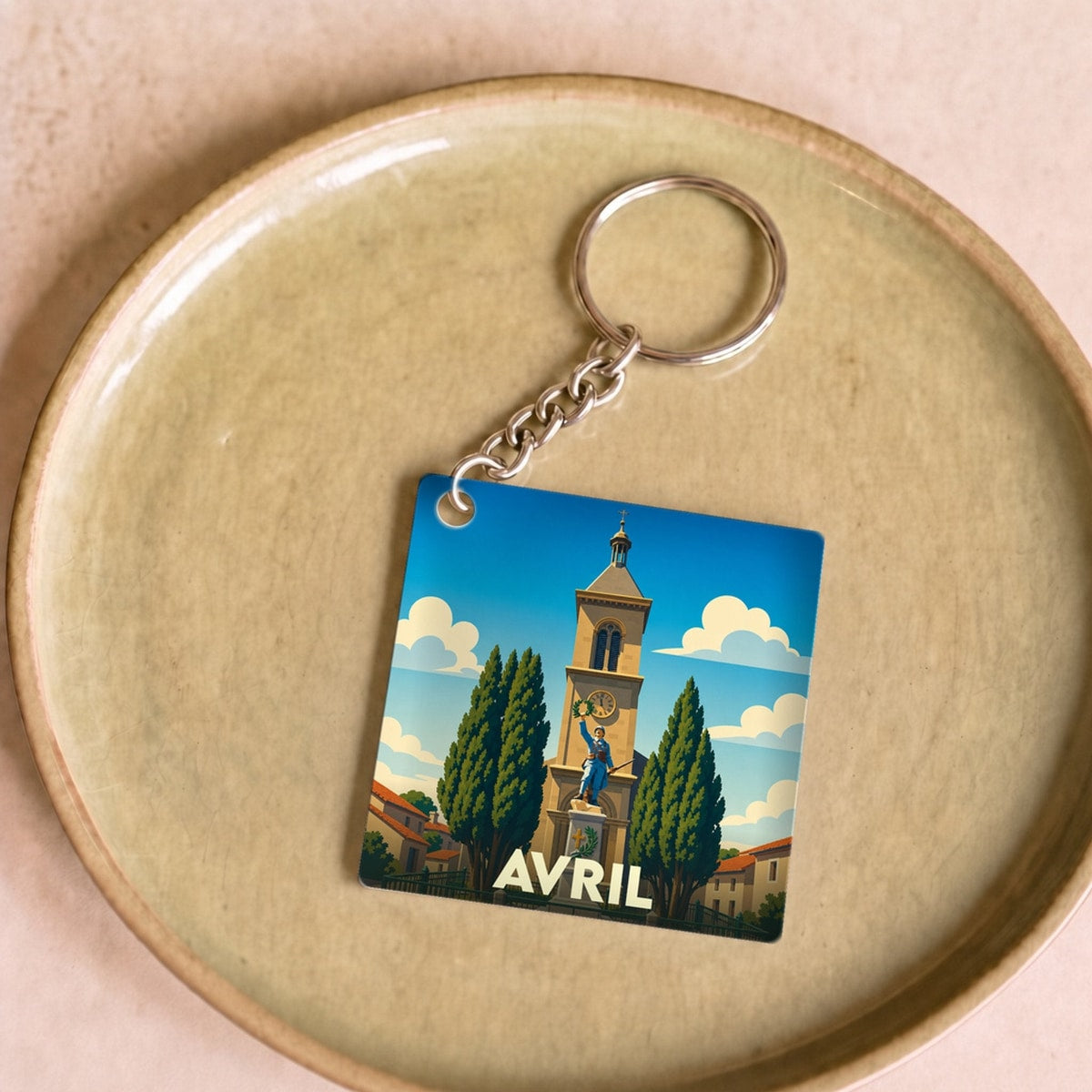 Porte-clés souvenir de la ville d'Avril avec une illustration stylisée de son monument aux morts et de son église.