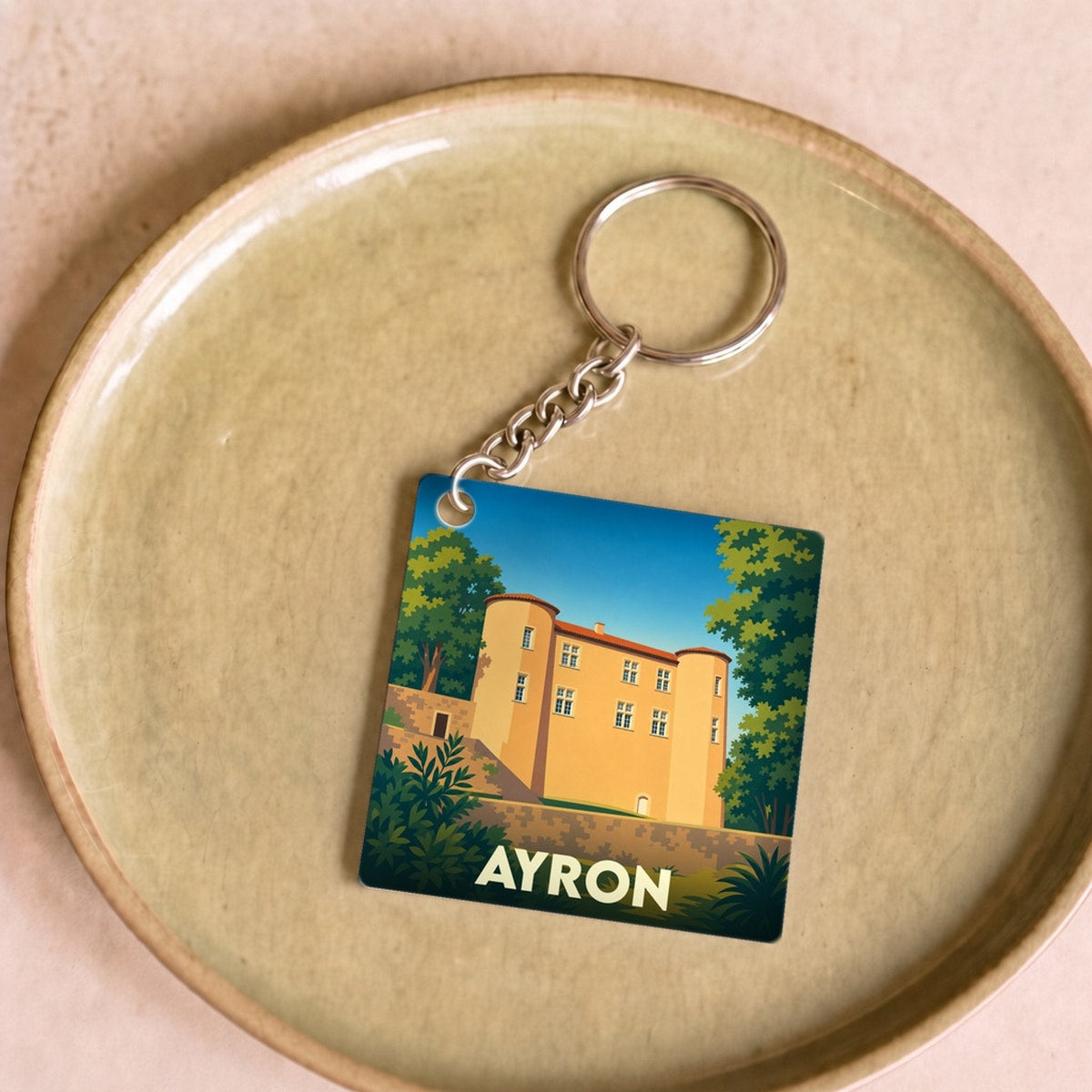 Porte-clés souvenir de la ville de Ayron avec une illustration stylisée du château local.
