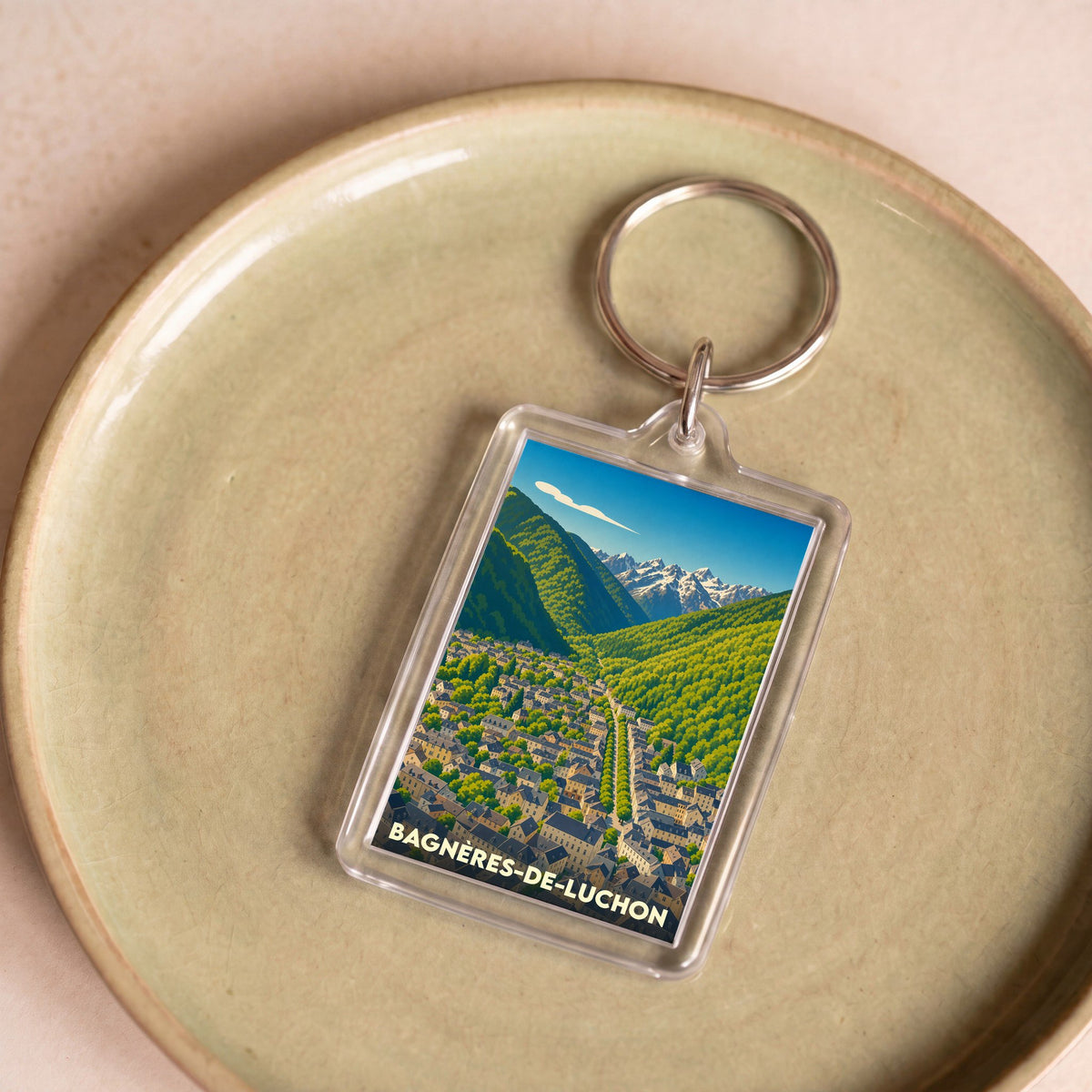 Porte-clés souvenir de la ville de Bagnères-de-Luchon avec une illustration stylisée de la vallée et des montagnes.