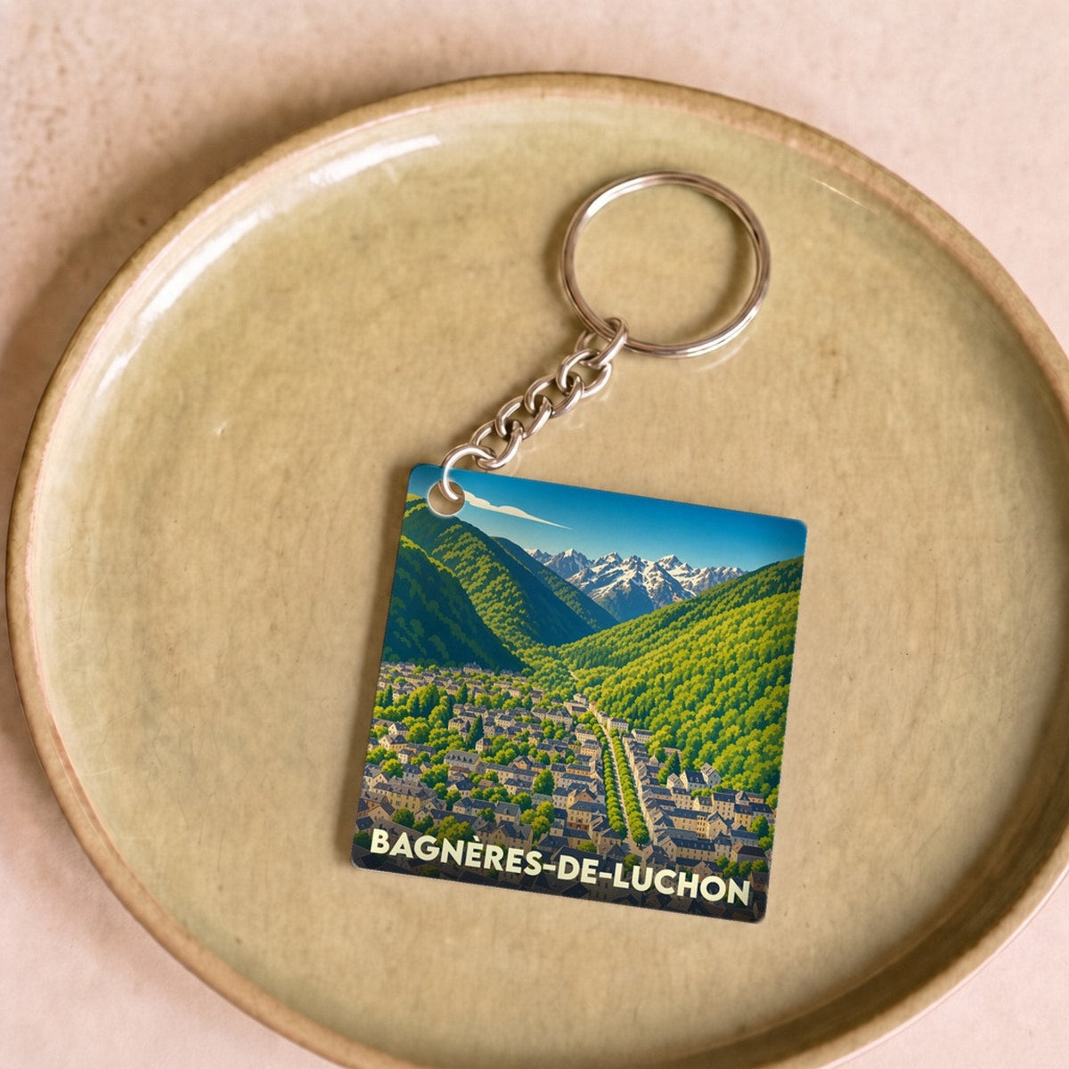 Porte-clés souvenir de la ville de Bagnères-de-Luchon avec une illustration stylisée de la vallée et des montagnes.