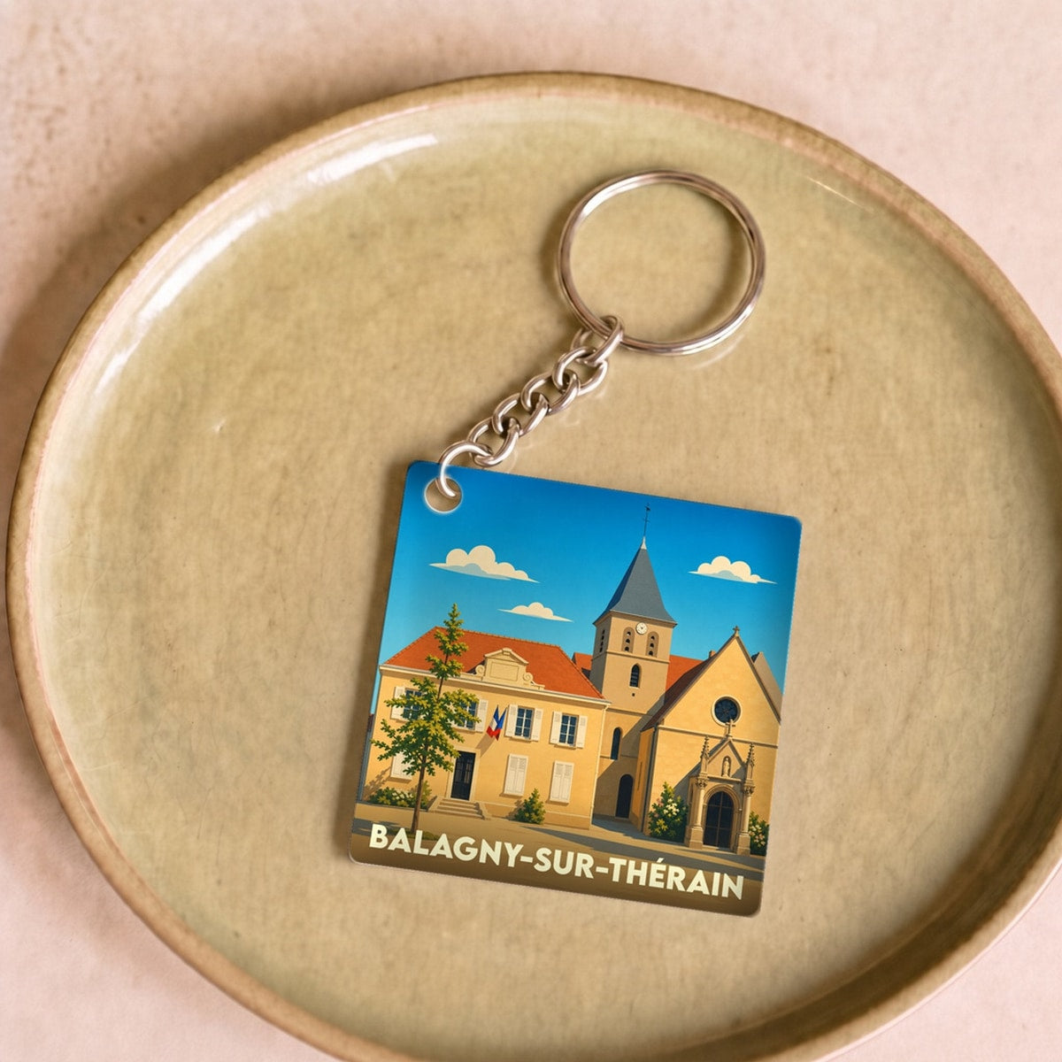 Porte-clés souvenir de la ville de Balagny-sur-Thérain avec une illustration stylisée de son église et de sa mairie.