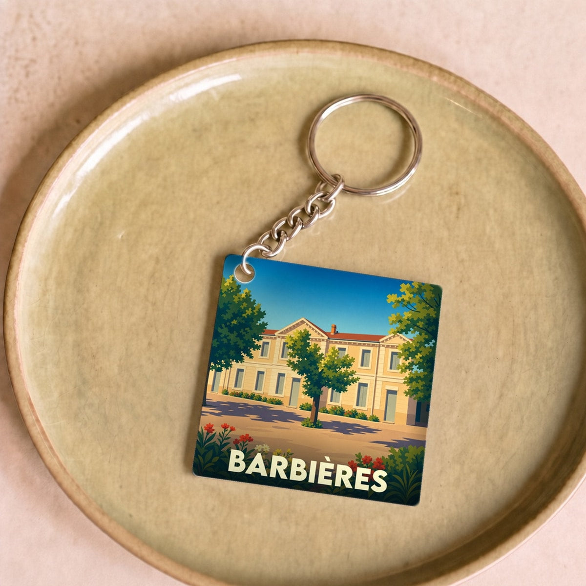 Porte-clés souvenir de la ville de Barbières avec une illustration stylisée d'un bâtiment ensoleillé.
