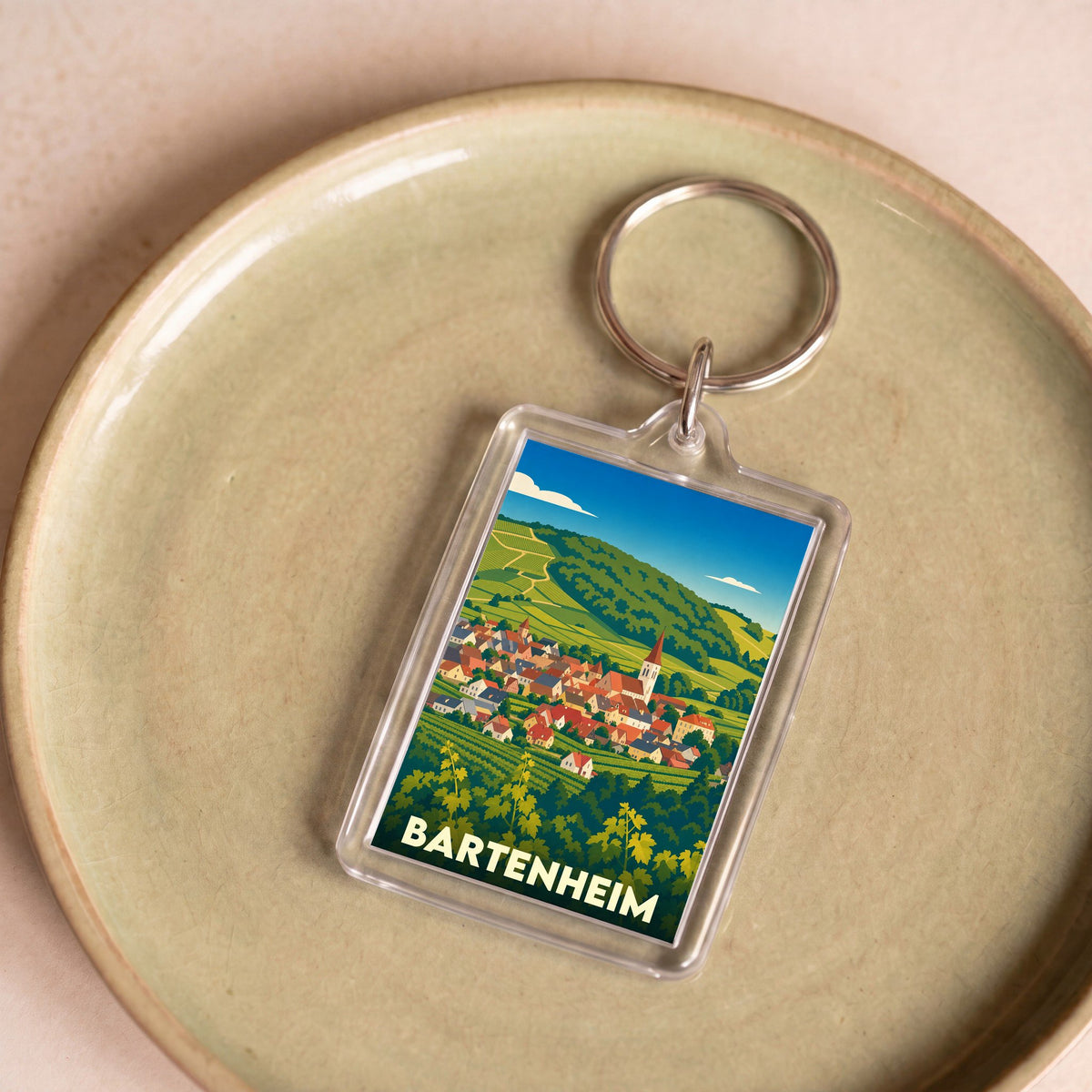 Porte-clés souvenir de la ville de Bartenheim avec une illustration stylisée de son paysage urbain et viticole.