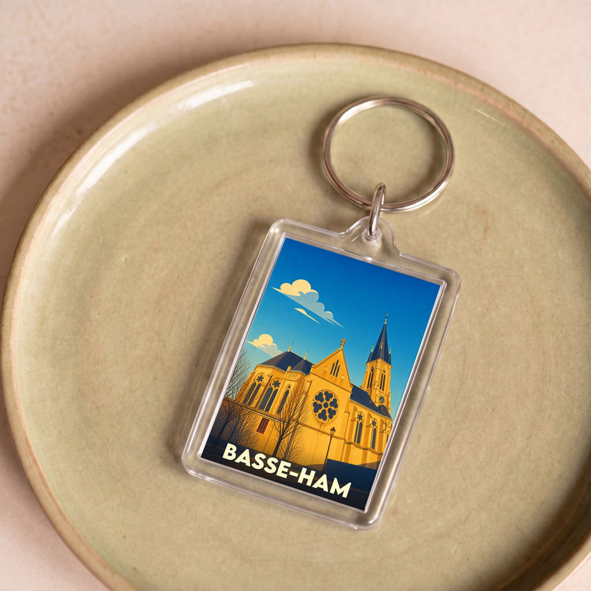 Porte-clés souvenir de la ville de Basse-Ham avec une illustration stylisée de son église sous un ciel bleu.