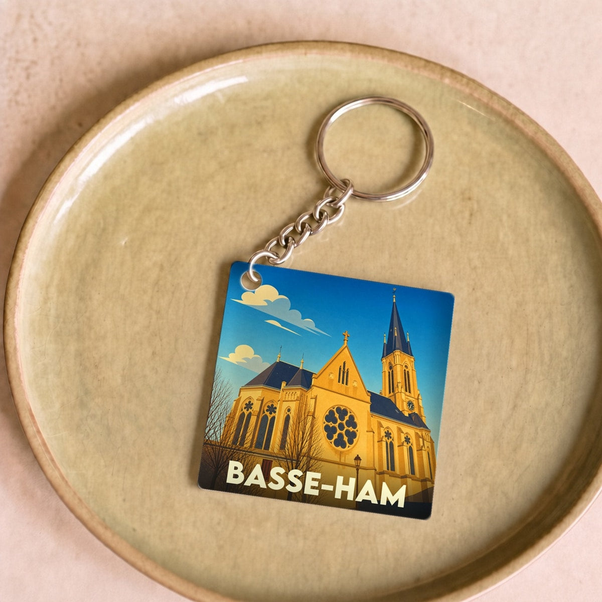 Porte-clés souvenir de la ville de Basse-Ham avec une illustration stylisée de son église sous un ciel bleu.