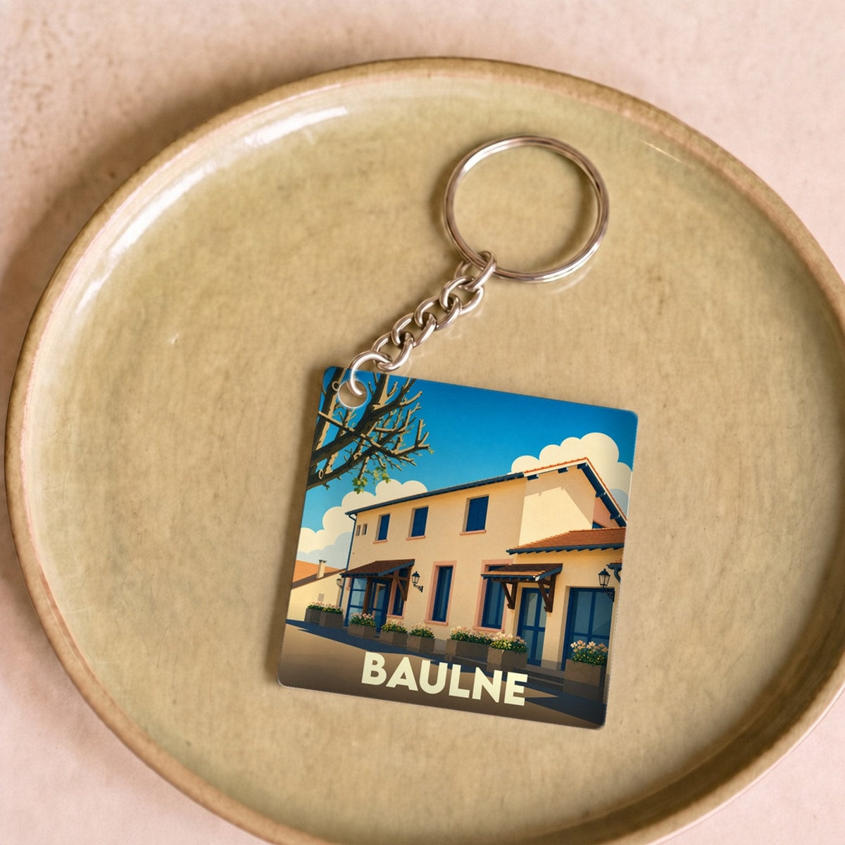 Porte-clés souvenir de la ville de Baulne avec une illustration stylisée d'un bâtiment ensoleillé.