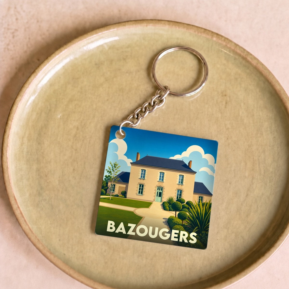Porte-clés souvenir de la ville de Bazougers avec une illustration stylisée d'une demeure traditionnelle.