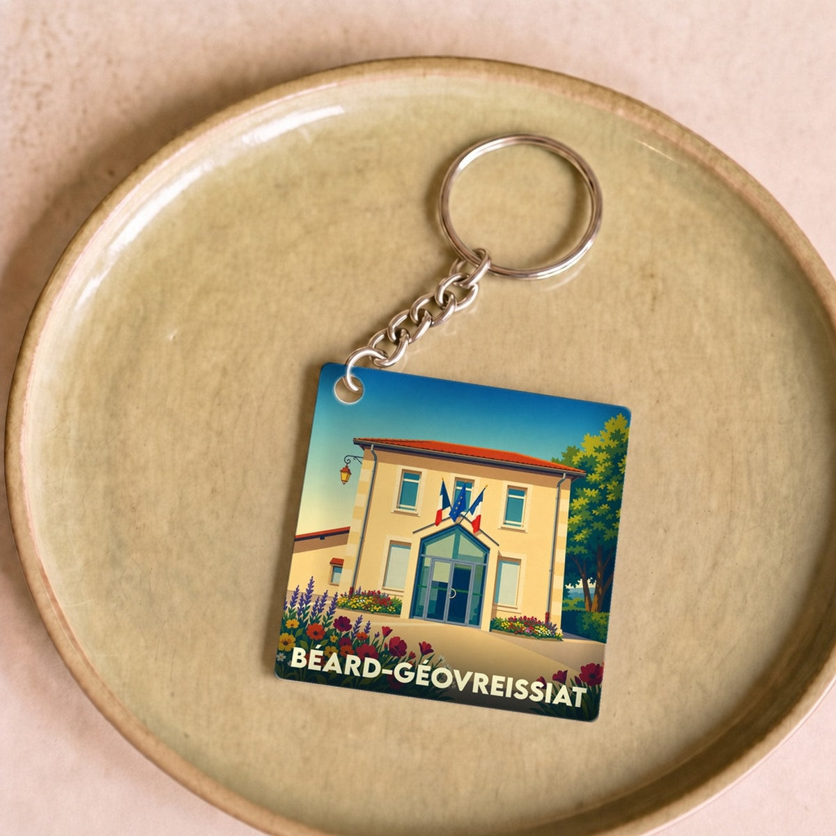Porte-clés souvenir de la ville de Béard-Géovreissiat avec une illustration stylisée de sa mairie fleurie.