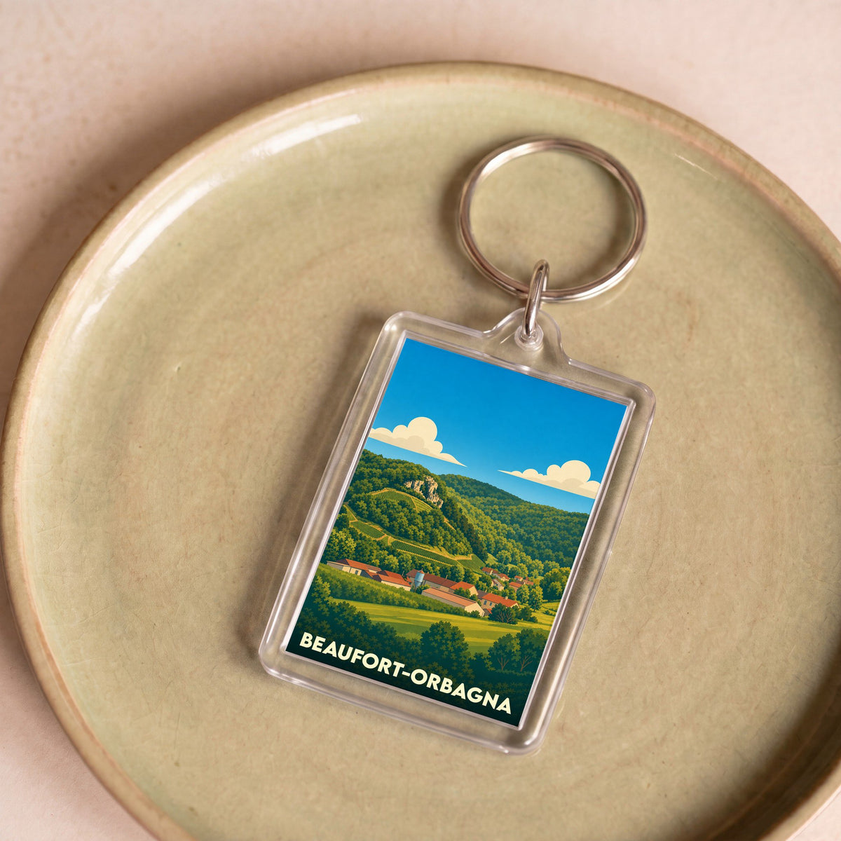 Porte-clés souvenir de Beaufort-Orbagna avec une illustration stylisée d'un paysage de campagne vallonné.