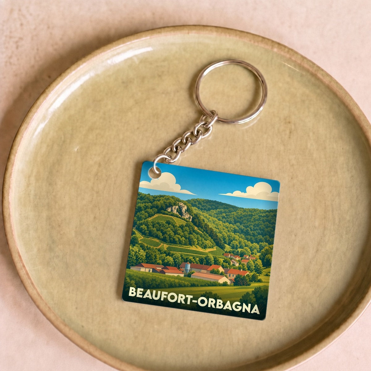 Porte-clés souvenir de Beaufort-Orbagna avec une illustration stylisée d'un paysage de campagne vallonné.