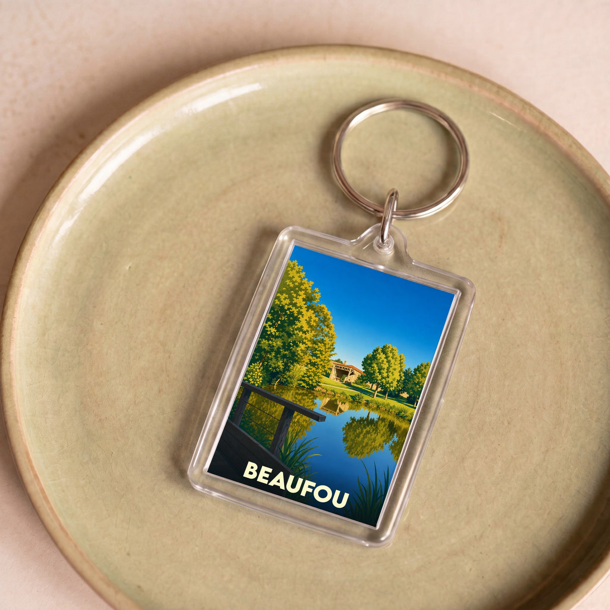 Porte-clés souvenir de la ville de Beaufou avec une illustration stylisée d'un paysage arboré au bord de l'eau.