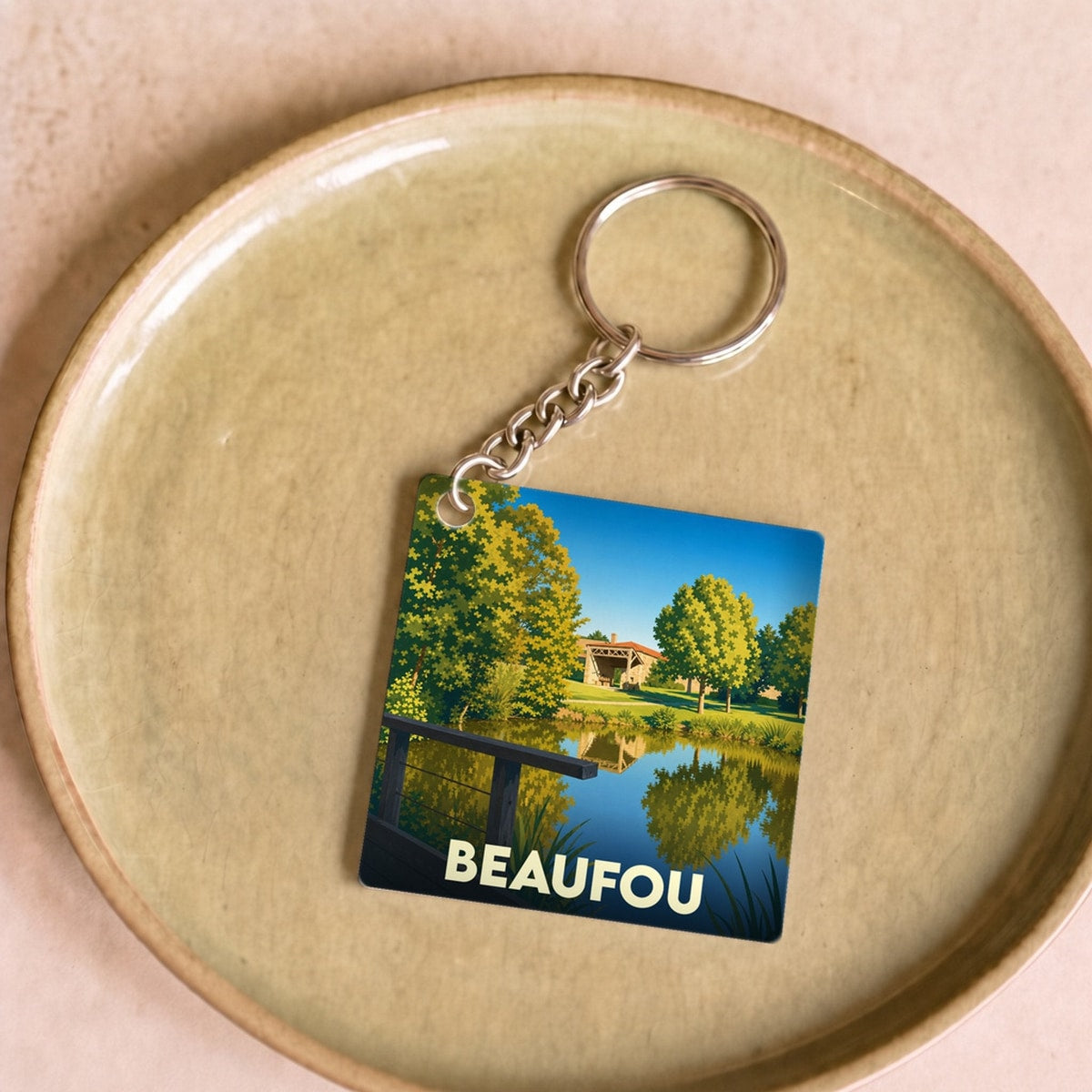 Porte-clés souvenir de la ville de Beaufou avec une illustration stylisée d'un paysage arboré au bord de l'eau.