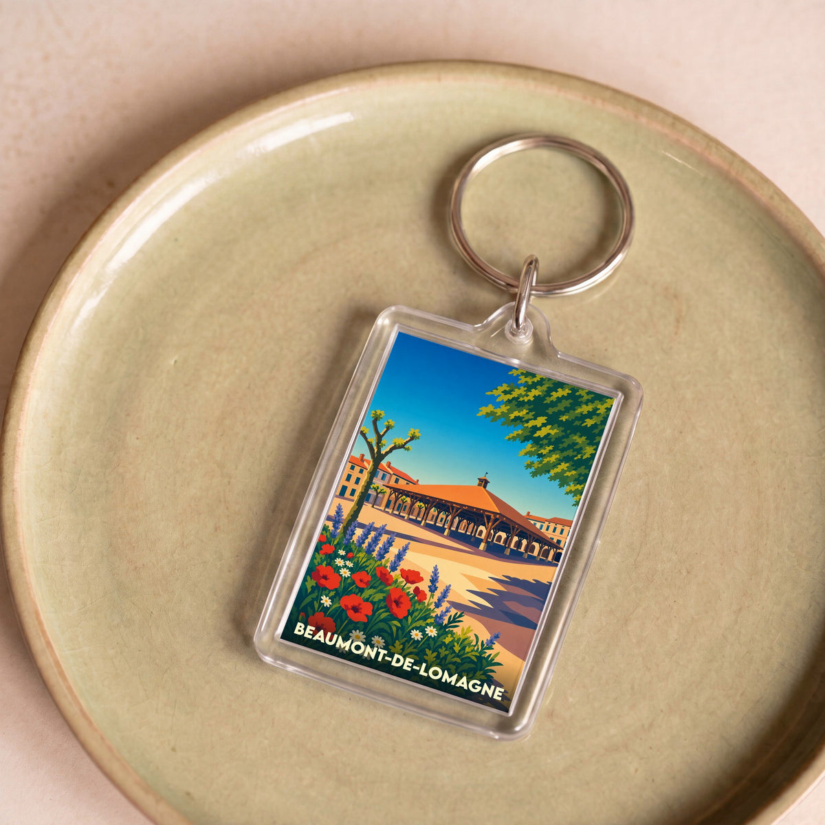 Porte-clés souvenir de la ville de Beaumont-de-Lomagne avec une illustration stylisée de sa halle et de fleurs champêtres.