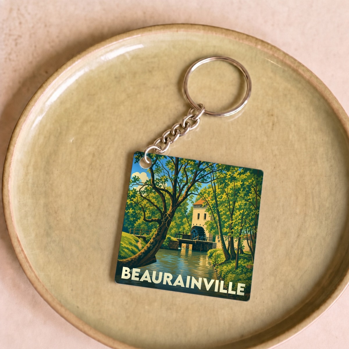 Porte-clés souvenir de la ville de Beaurainville avec une illustration stylisée d'un moulin au bord de l'eau.