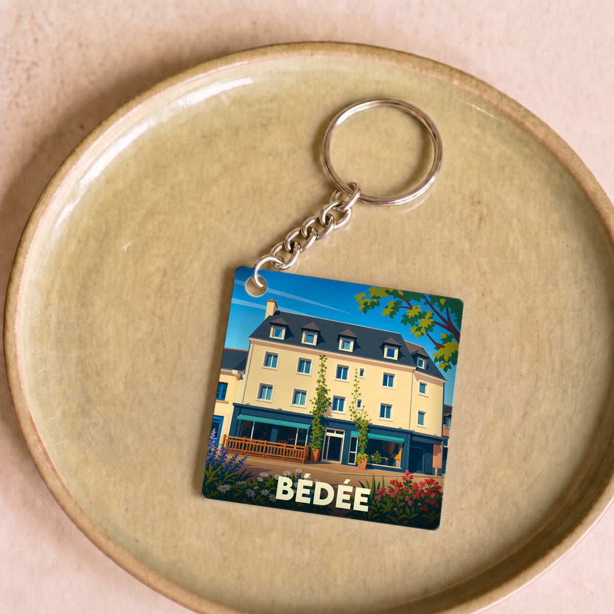 Porte-clés souvenir de la ville de Bédée avec une illustration stylisée d'un bâtiment fleuri.