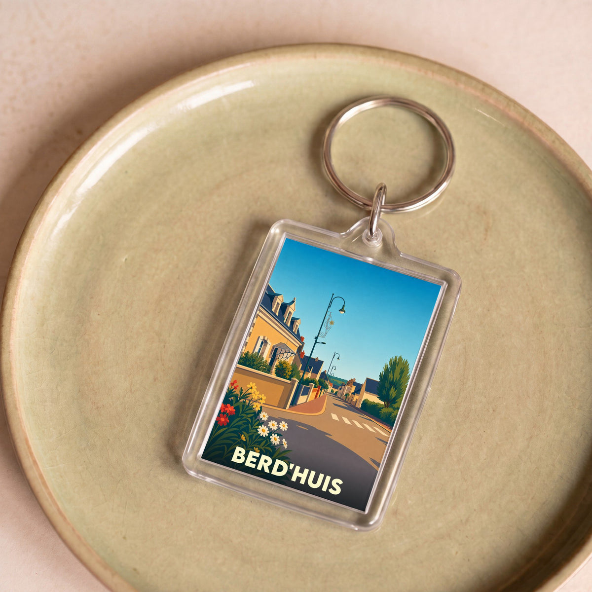 Porte-clés souvenir de la ville de Berd'huis avec une illustration stylisée d'une rue ensoleillée.