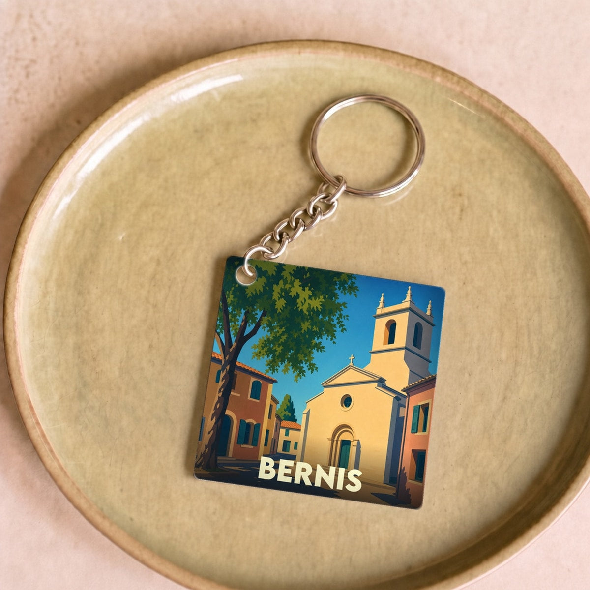 Porte-clés souvenir de la ville de Bernis avec une illustration stylisée d'une place ensoleillée.