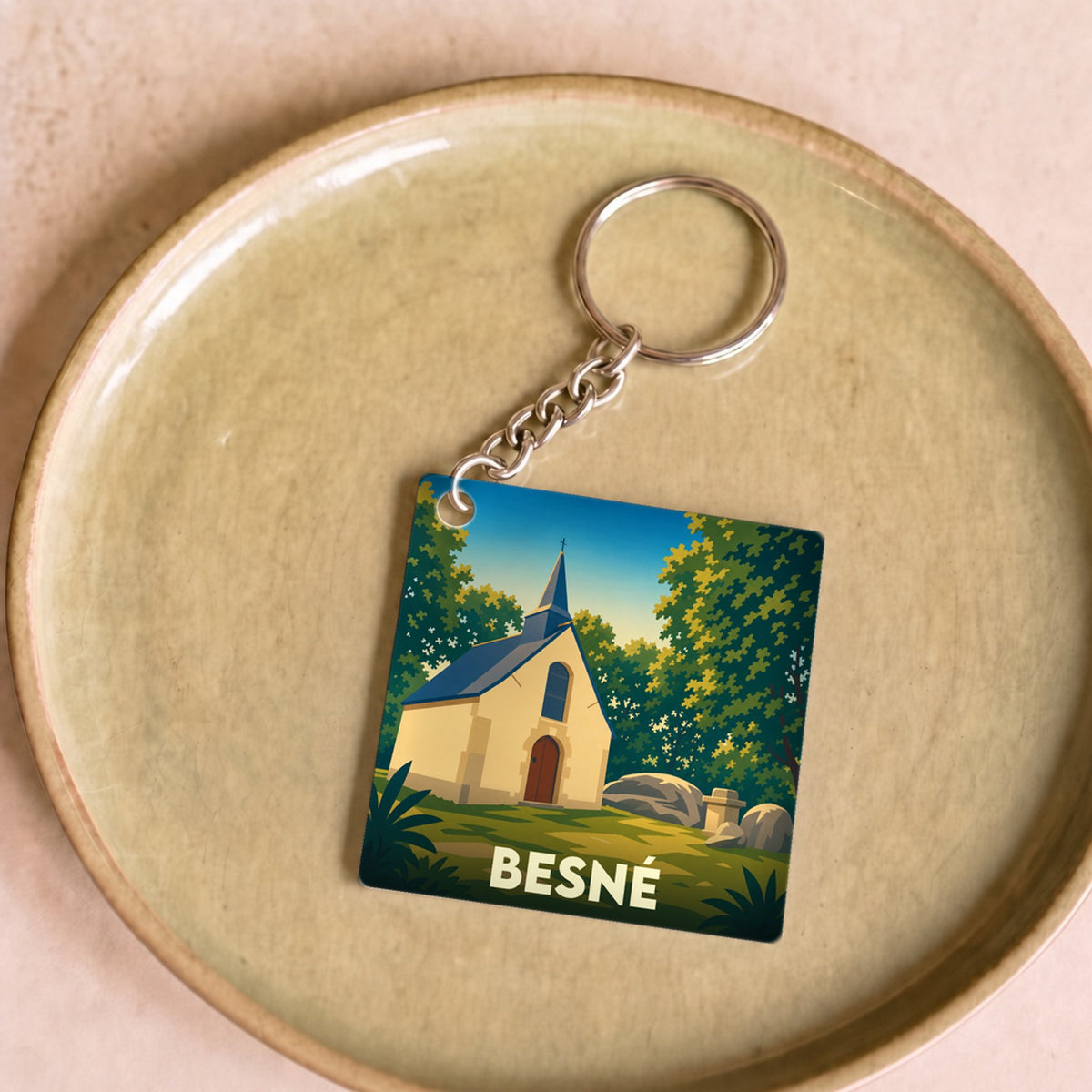 Porte-clés souvenir de la ville de Besné avec une illustration stylisée d'une chapelle en pleine nature.