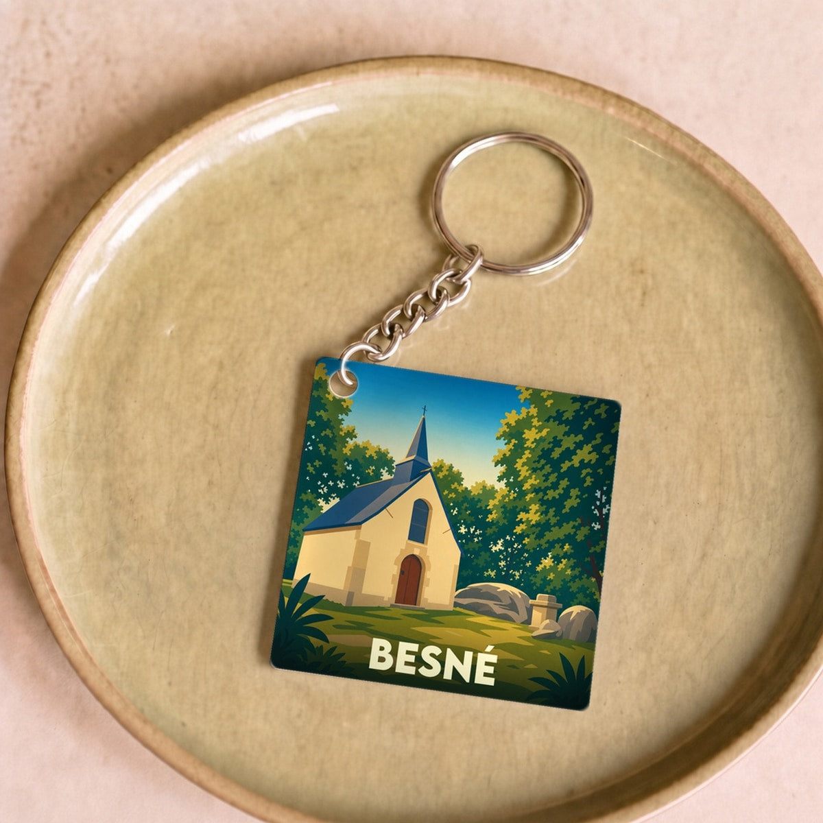 Porte-clés souvenir de la ville de Besné avec une illustration stylisée d'une chapelle en pleine nature.