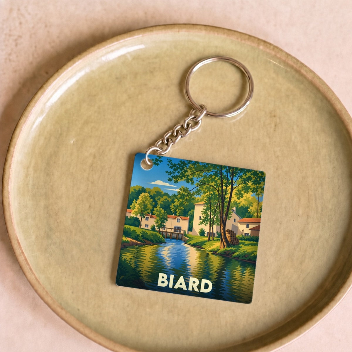 Porte-clés souvenir de la ville de Biard avec une illustration stylisée d'un paysage de rivière.