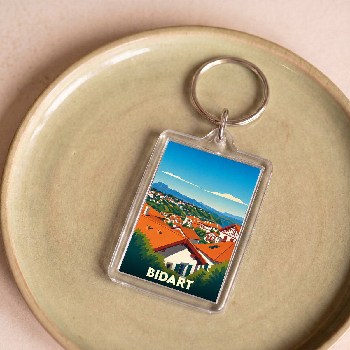 Porte-clés souvenir de la ville de Bidart avec une illustration stylisée de ses toits rouges face aux montagnes.