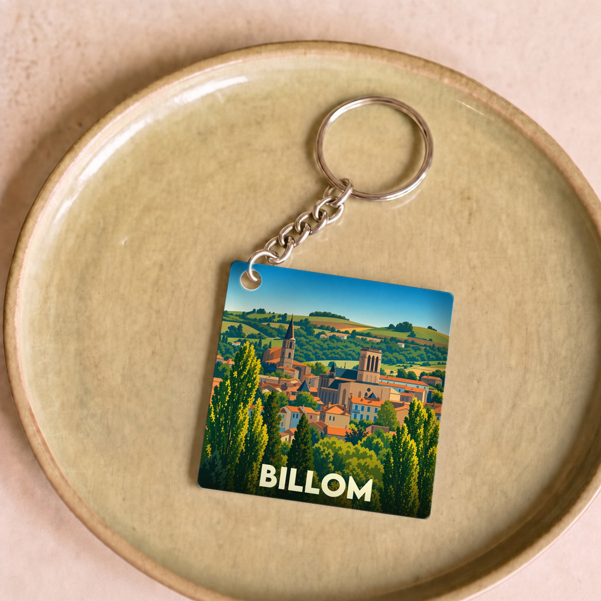 Porte-clés souvenir de la ville de Billom orné d'une illustration stylisée du paysage urbain et de sa campagne.
