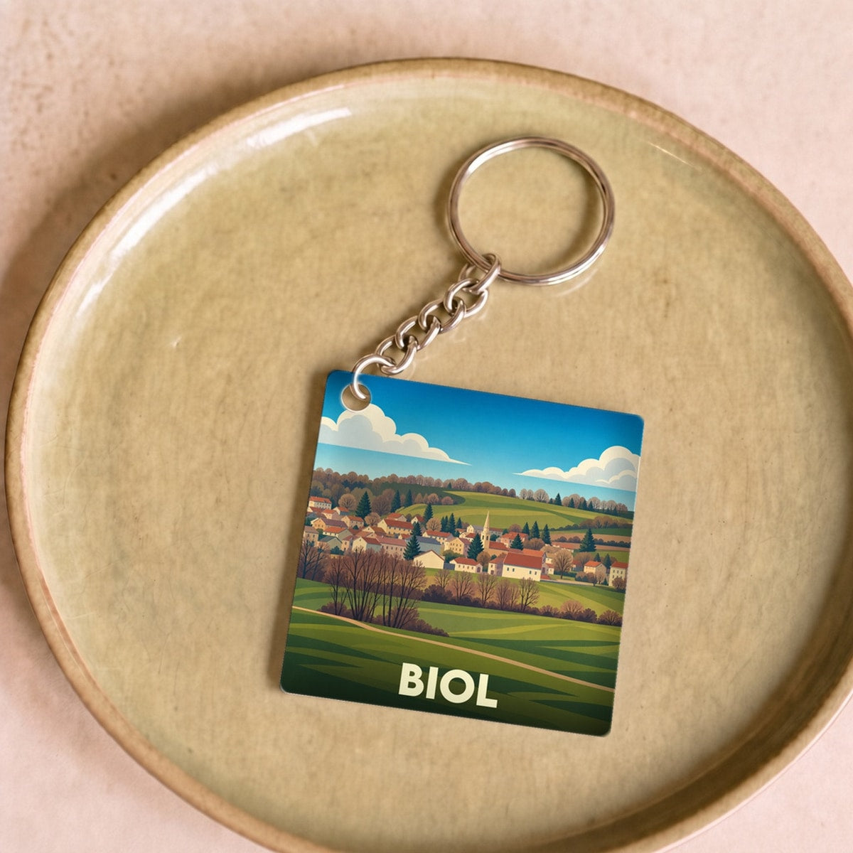Porte-clés souvenir de la ville de Biol avec une illustration stylisée de son paysage vallonné.