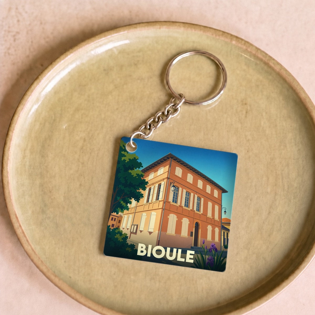 Porte-clés souvenir de la ville de Bioule avec une illustration stylisée d'un bâtiment historique.