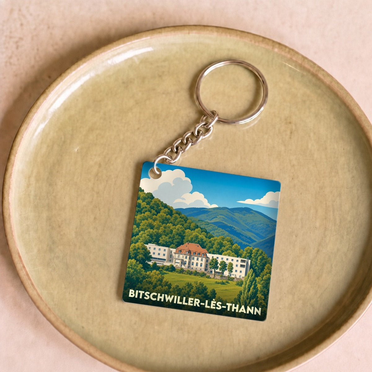 Porte-clés souvenir de la ville de Bitschwiller-lès-Thann avec une illustration stylisée d'un bâtiment dans un paysage de montagne.