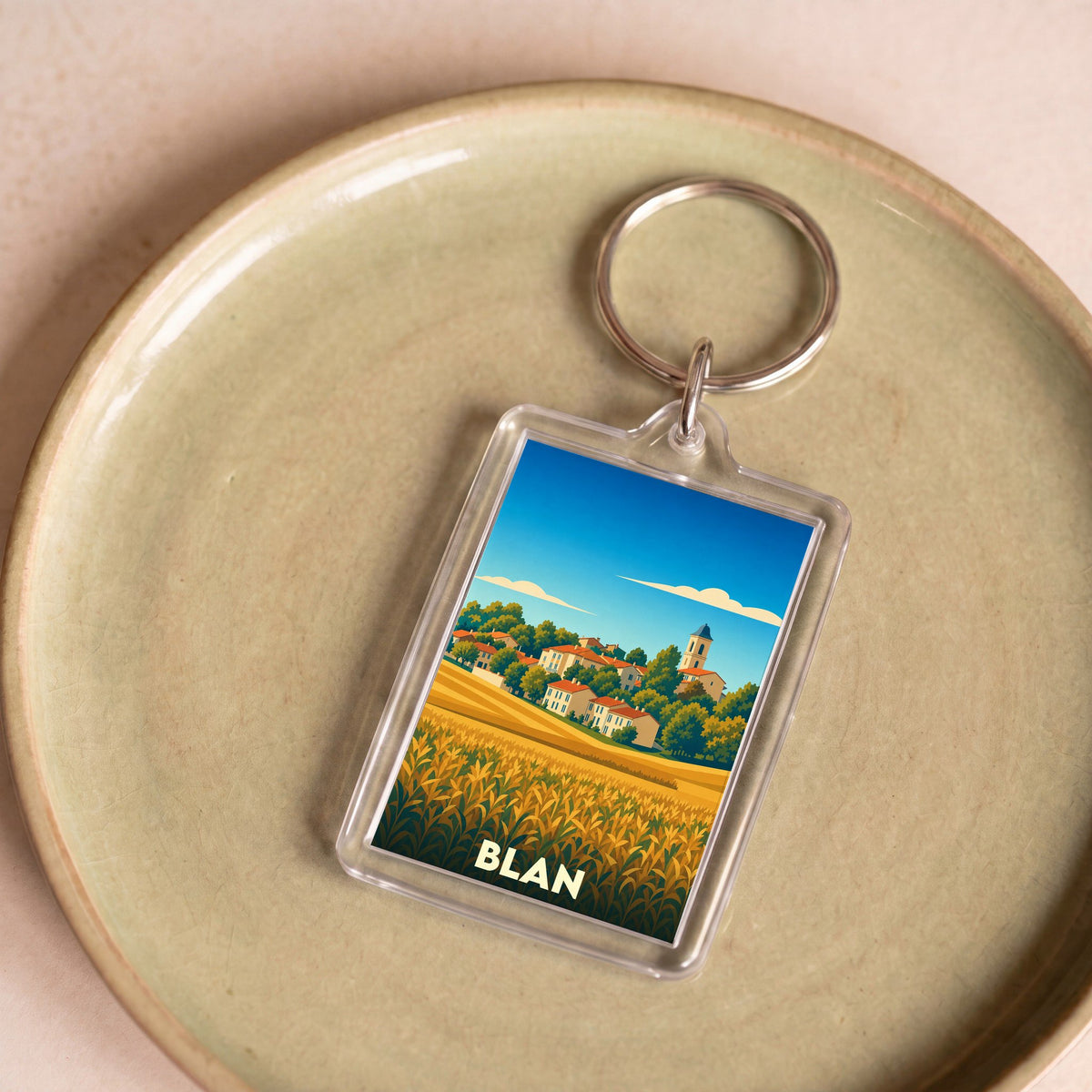Porte-clés souvenir de la ville de Blan avec une illustration stylisée d'un village et de champs.