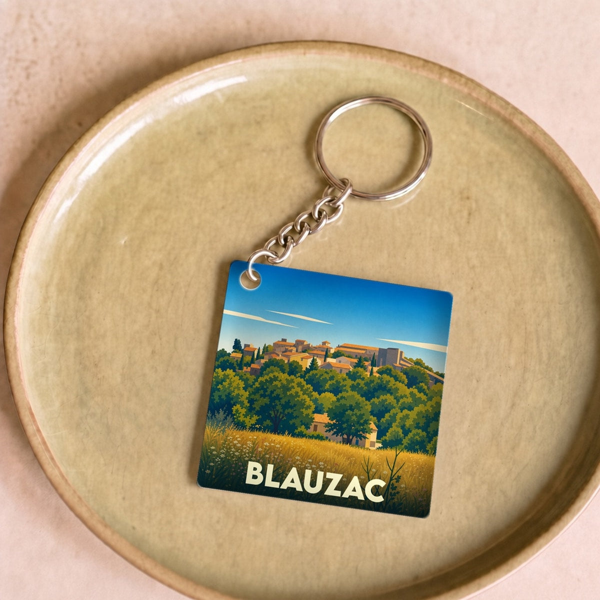 Porte-clés souvenir de la ville de Blauzac avec une illustration stylisée de son paysage provençal.