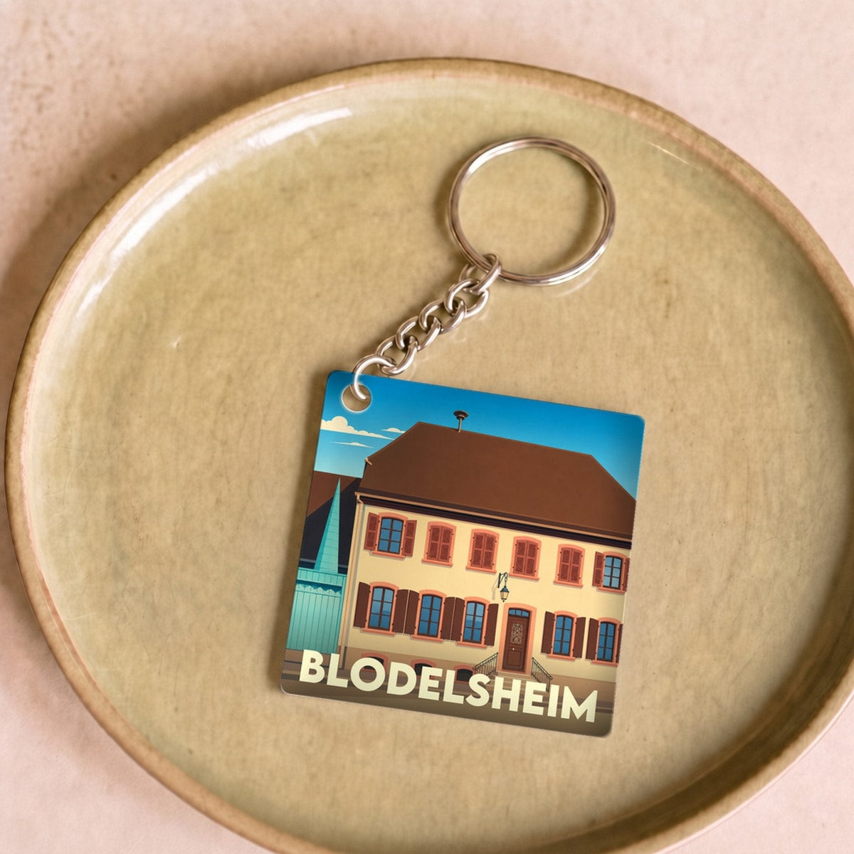 Porte-clés souvenir de la ville de Blodelsheim avec une illustration stylisée d'un bâtiment traditionnel.