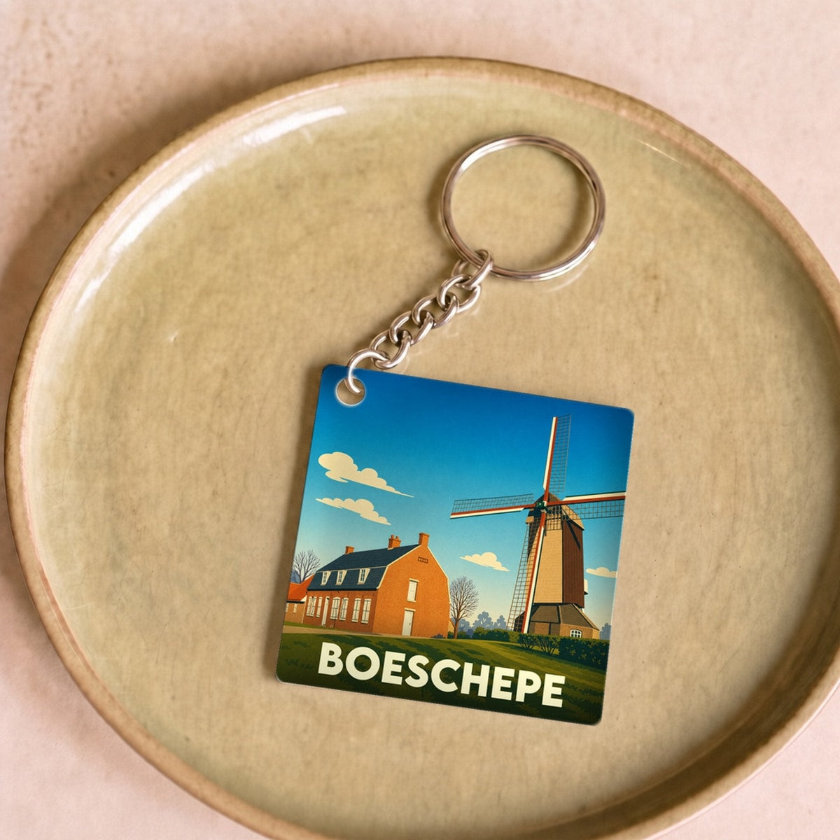 Porte-clés souvenir de la ville de Boeschepe avec une illustration stylisée d'un moulin et d'une maison flamande.