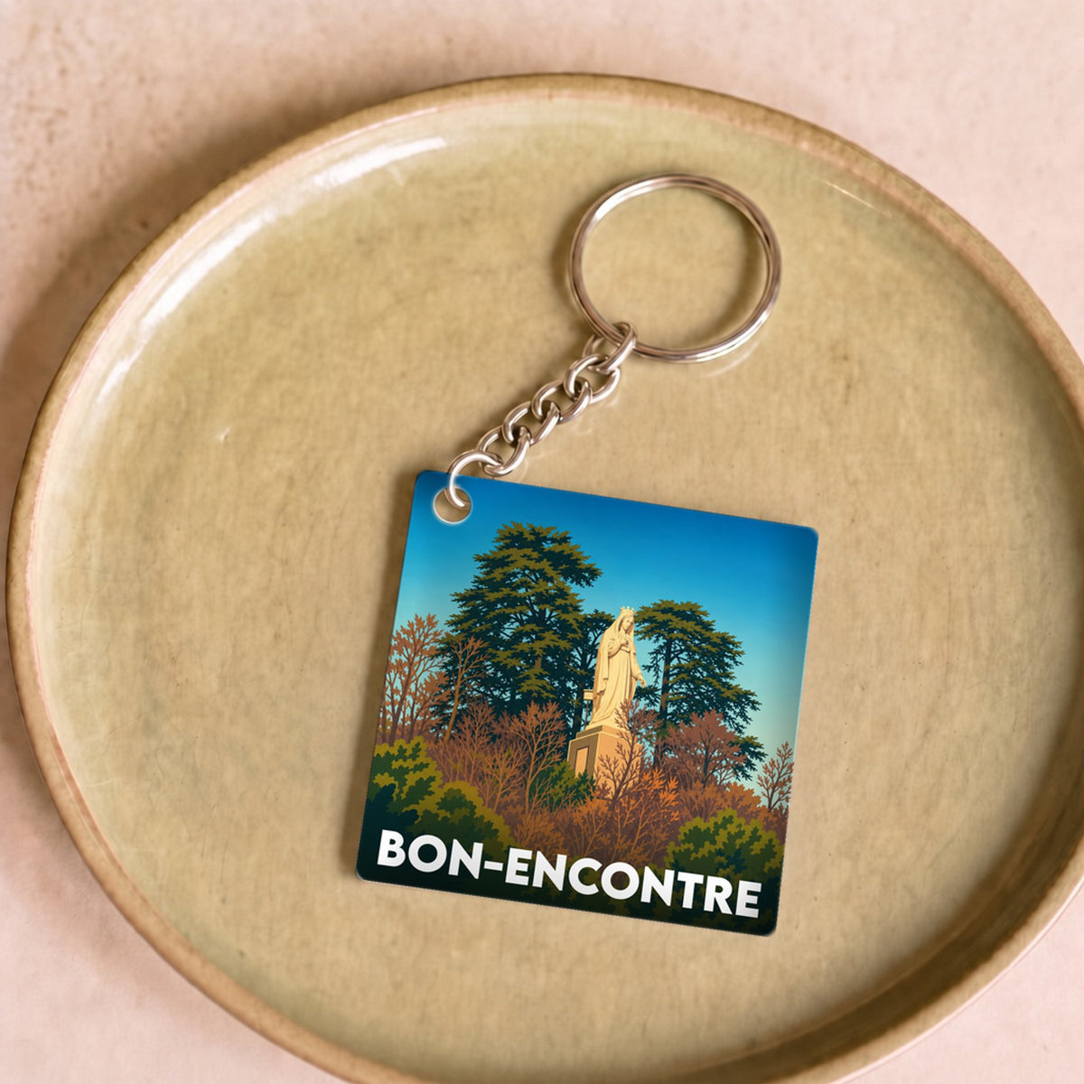 Porte-clés souvenir de la ville de Bon-Encontre avec une illustration stylisée d'une statue parmi les arbres.