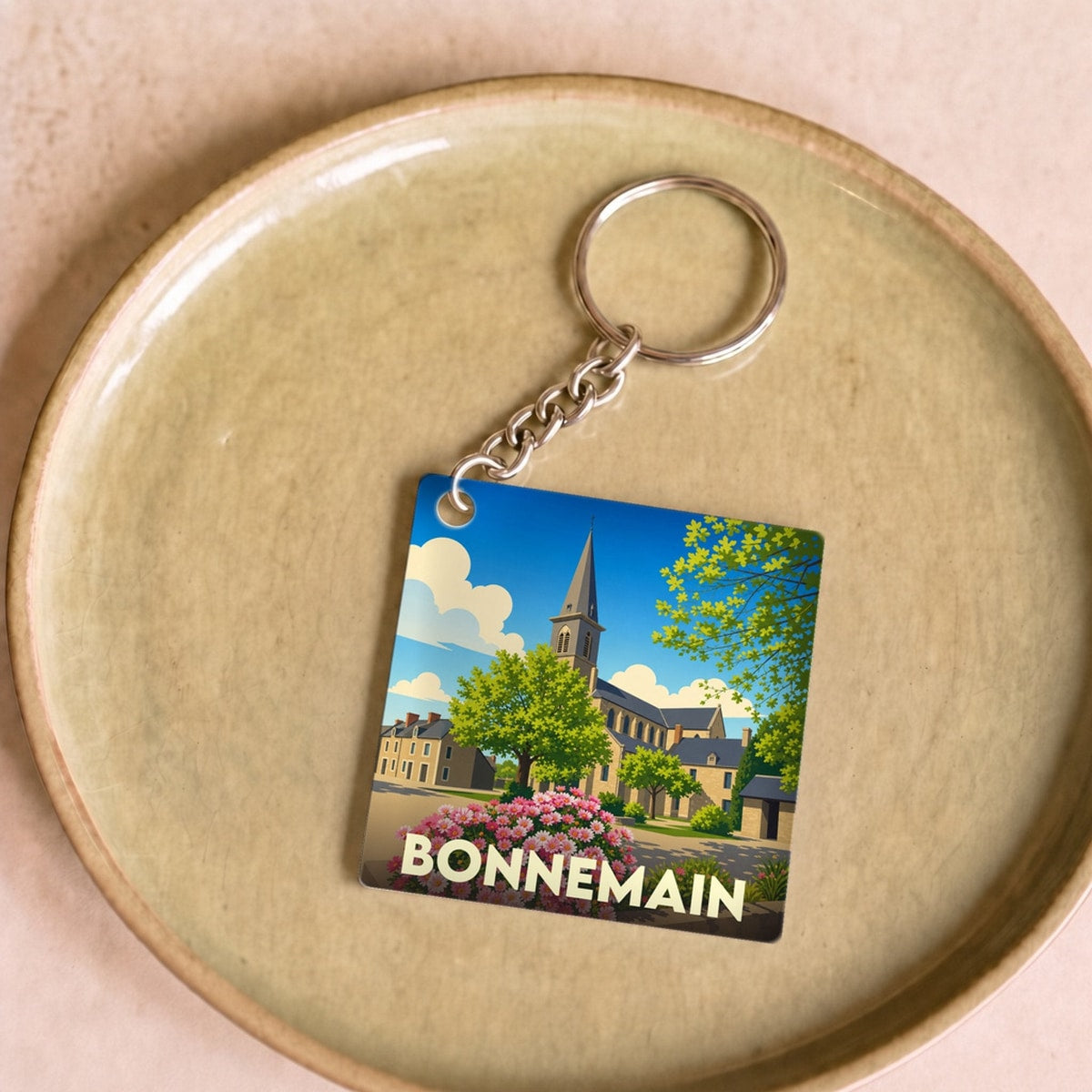 Porte-clés souvenir de la ville de Bonnemain avec une illustration stylisée de son église et de parterres fleuris.