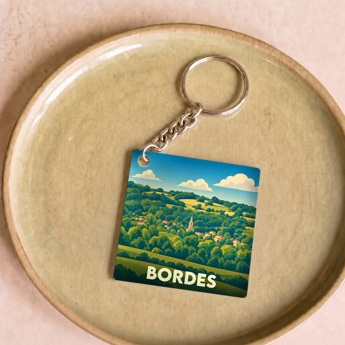 Porte-clés souvenir de la ville de Bordes avec une illustration stylisée d'un paysage vallonné.