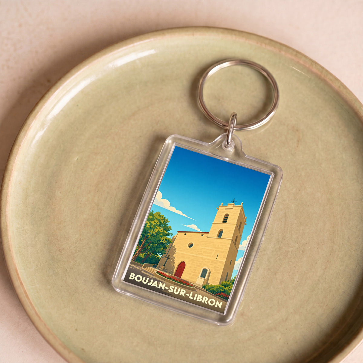 Porte-clés souvenir de la ville de Boujan-sur-Libron avec une illustration stylisée de son église.