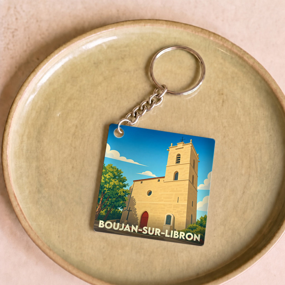 Porte-clés souvenir de la ville de Boujan-sur-Libron avec une illustration stylisée de son église.