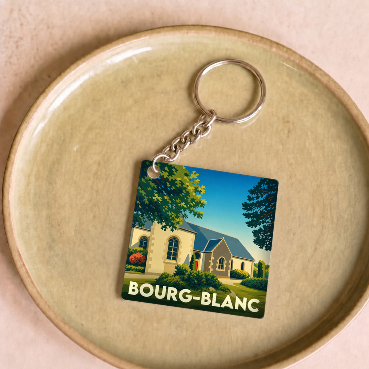 Porte-clés souvenir de la ville de Bourg-Blanc avec une illustration stylisée d'une église sous un ciel bleu.