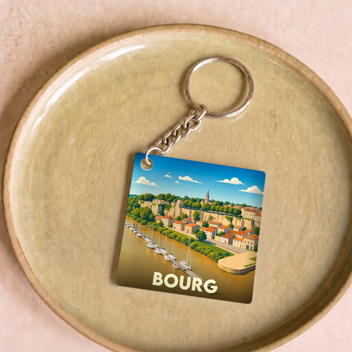 Porte-clés souvenir de la ville de Bourg avec une illustration stylisée d'un port au pied d'une falaise.