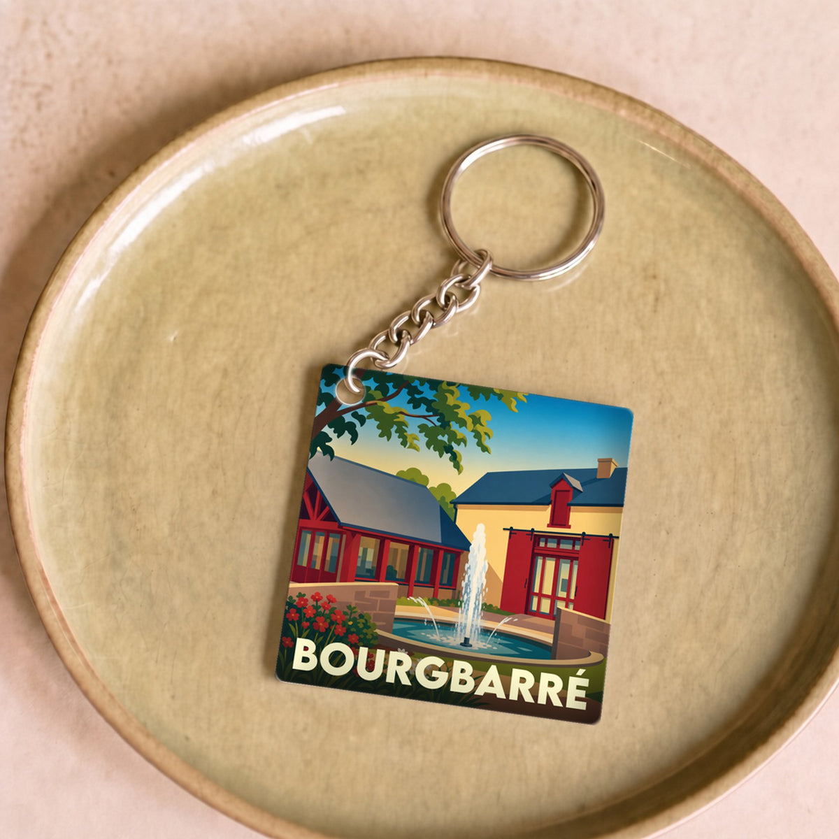 Porte-clés souvenir de la ville de Bourgbarré avec une illustration stylisée d'une fontaine et de bâtiments colorés.