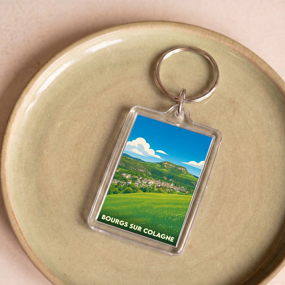 Porte-clés souvenir de la ville de Bourgs sur Colagne avec une illustration paysagère stylisée.