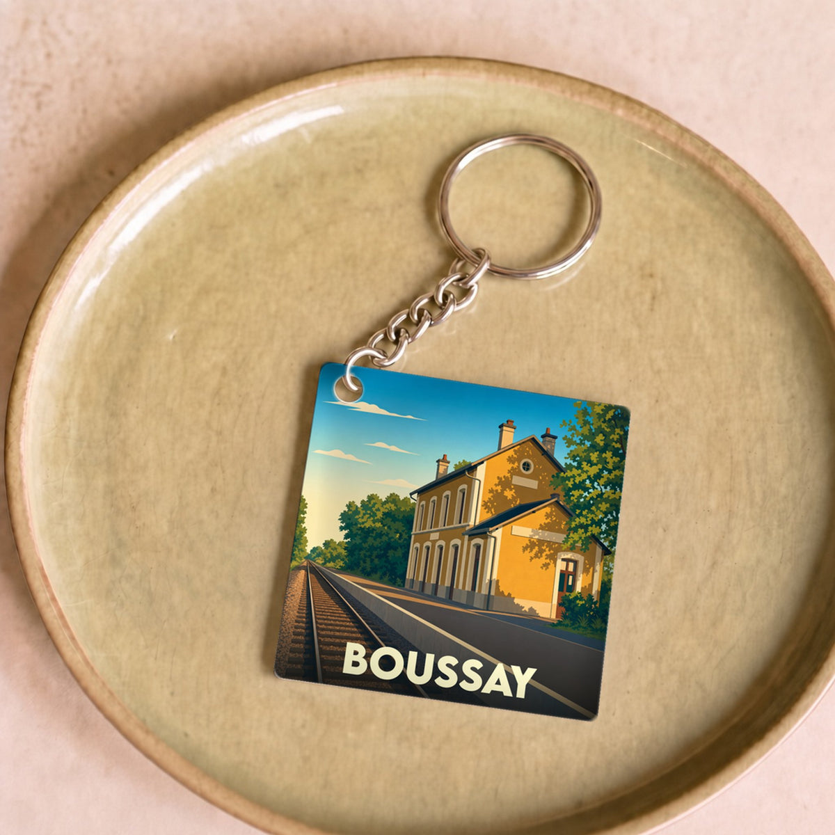 Porte-clés souvenir de la ville de Boussay avec une illustration stylisée d'une gare sous un ciel bleu.